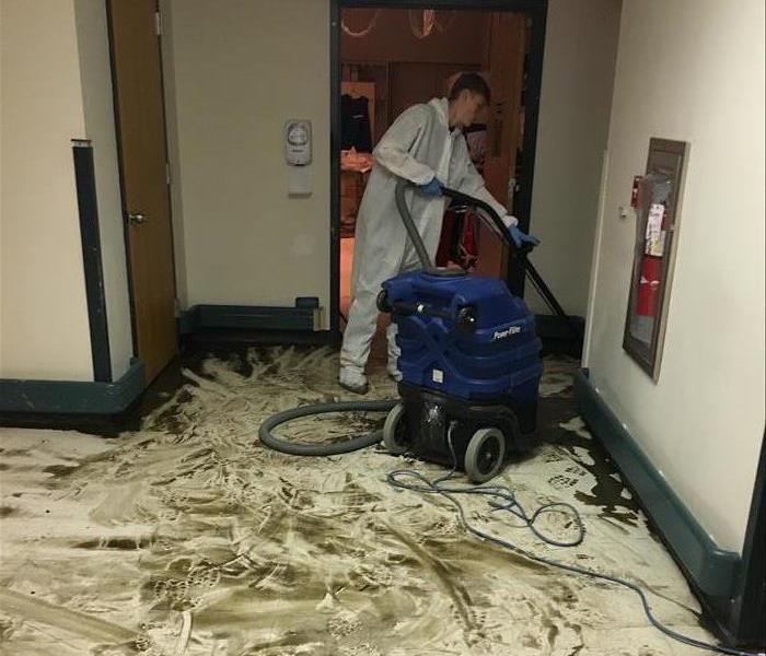 A water damaged floor with SERVPRO employee cleaning it up
