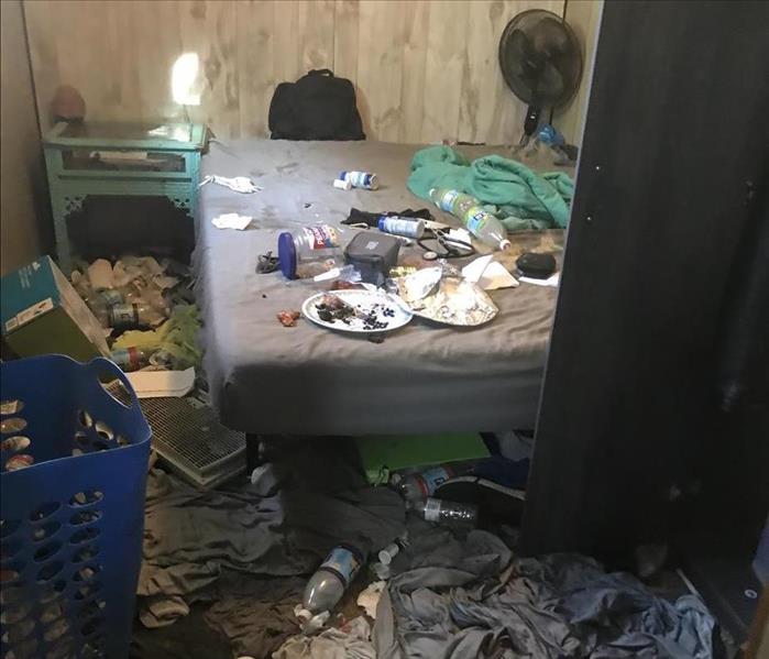 A bedroom in disarray with clothes and old food in it
